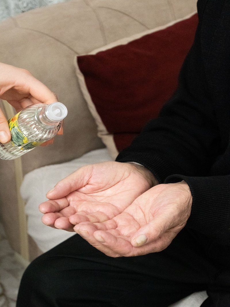 Manos de una cuidadora aplicando alcohol a las manos de una abuela, en un cuidado cotidiano y con dignidad